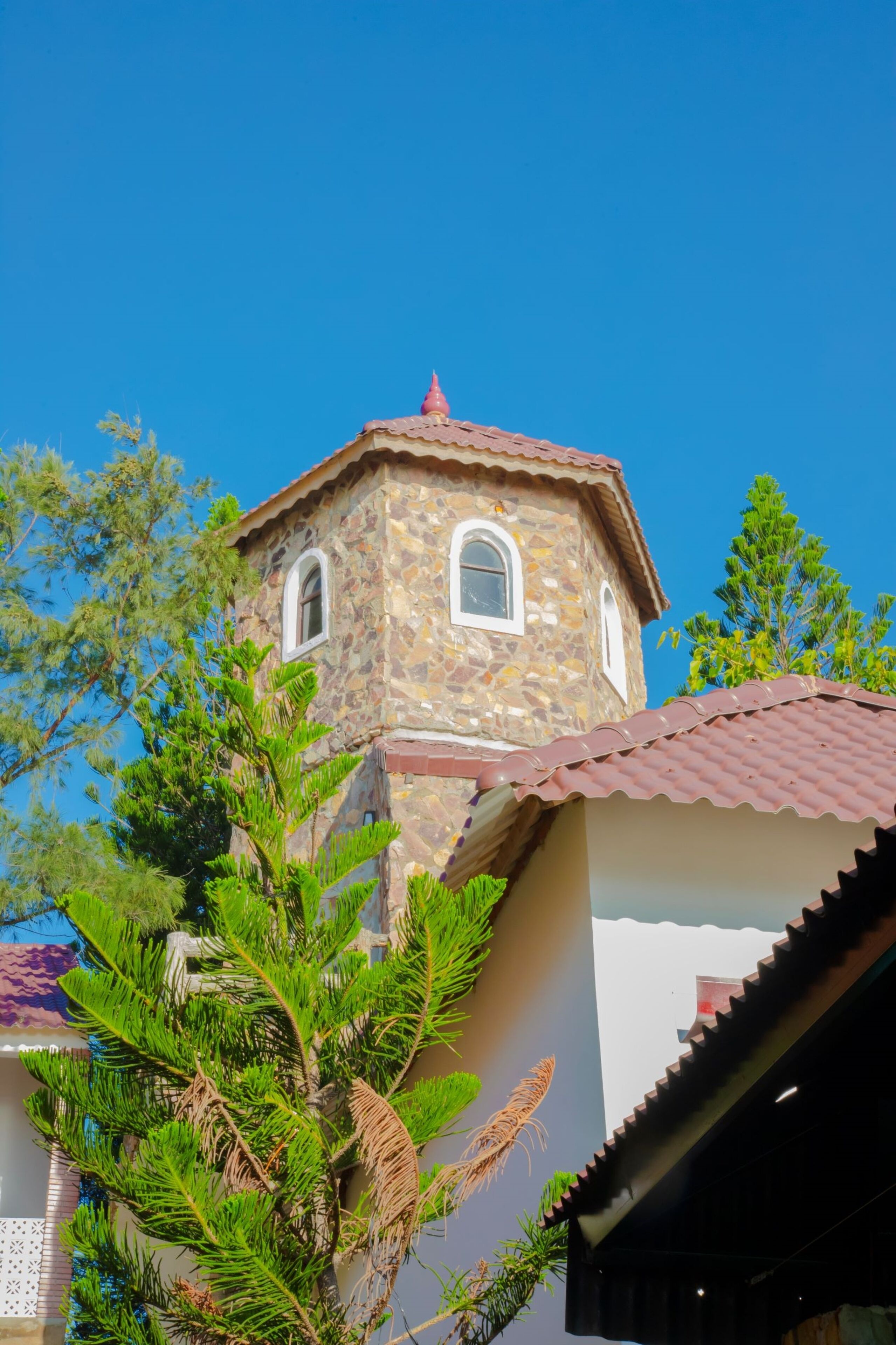 A stone building with a red-tiled roof and arched windows, surrounded by greenery.