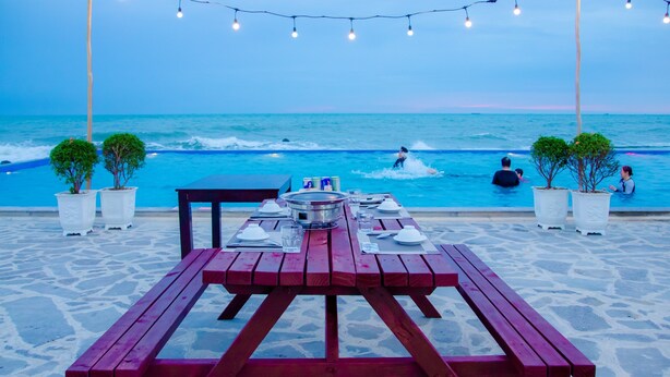 Un espace de restauration aménagé au bord de la plage, avec une table dressée pour deux personnes, offrant une vue sur l’océan.