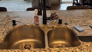 A kitchen with granite countertops, stainless steel sinks, and a view of the backyard through large windows.