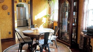 Un comedor con una mesa redonda, sillas, un refrigerador al fondo y un mueble con puertas de vidrio.
