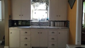 Una cocina con armarios blancos, un lavamanos y una ventana con cortinas.