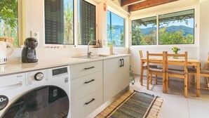 A kitchen with a washing machine, wooden dining table, and large windows offering a mountain view.