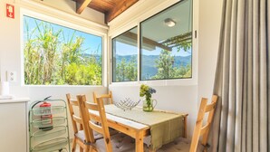 A dining area with a table, chairs, a fire extinguisher, and a window with a view of greenery and hills.