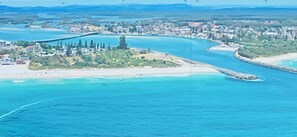 An aerial view of a coastal town with a prominent bridge, clear blue waters, and a mix of residential and commercial buildings.
