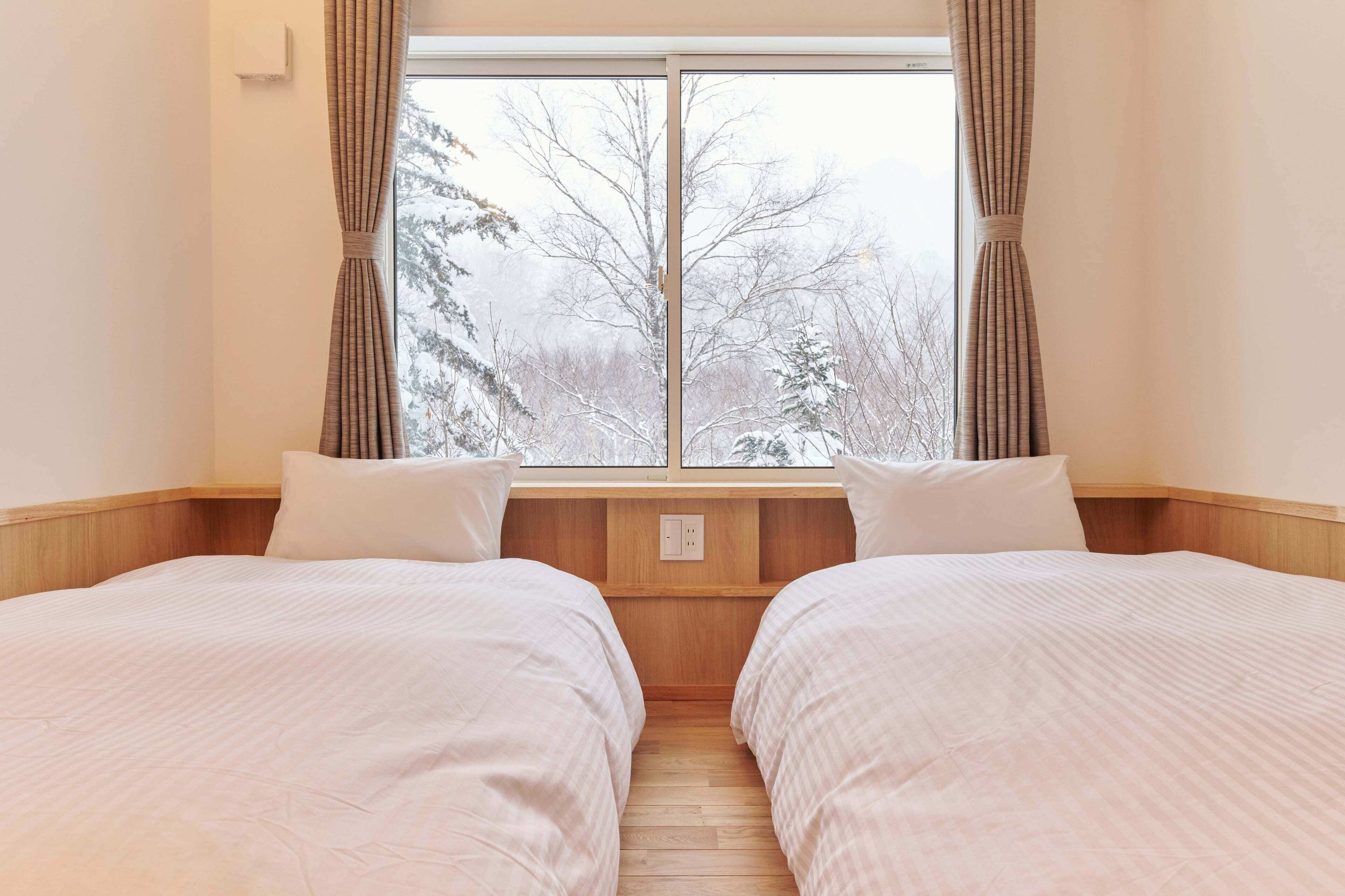 Una habitación con dos camas, una ventana con cortinas y vistas a árboles cubiertos de nieve.