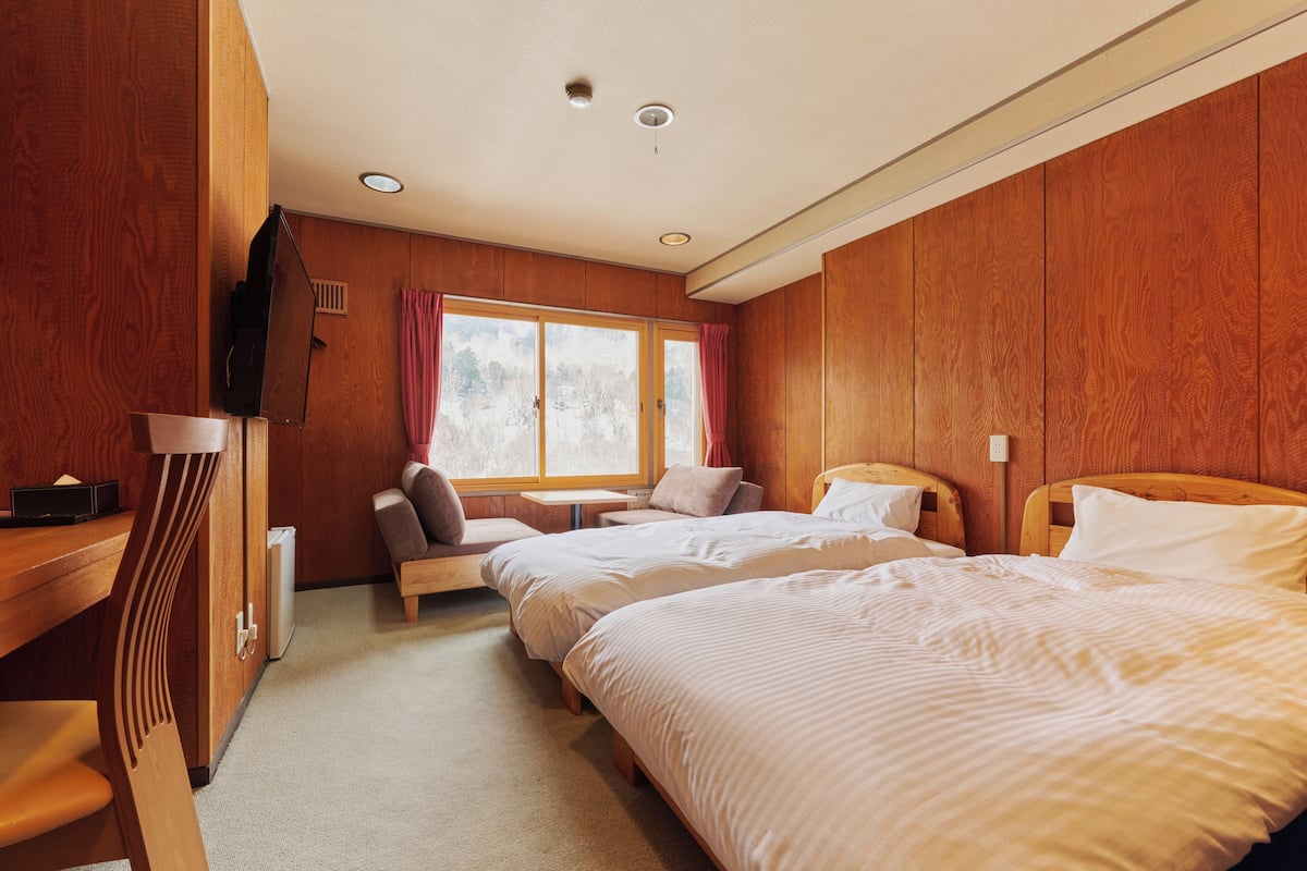 Una camera d'albergo con pannelli in legno, due letti, una scrivania e una finestra con tende.
