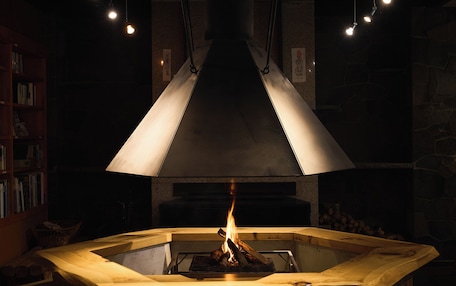 A wood-burning stove with a large, conical chimney, surrounded by bookshelves and a stone wall.