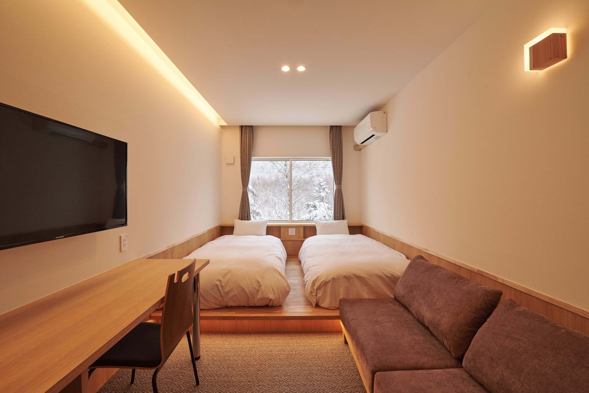 Una camera d'albergo con un letto, una scrivania, una sedia, una televisione e una finestra con tende.