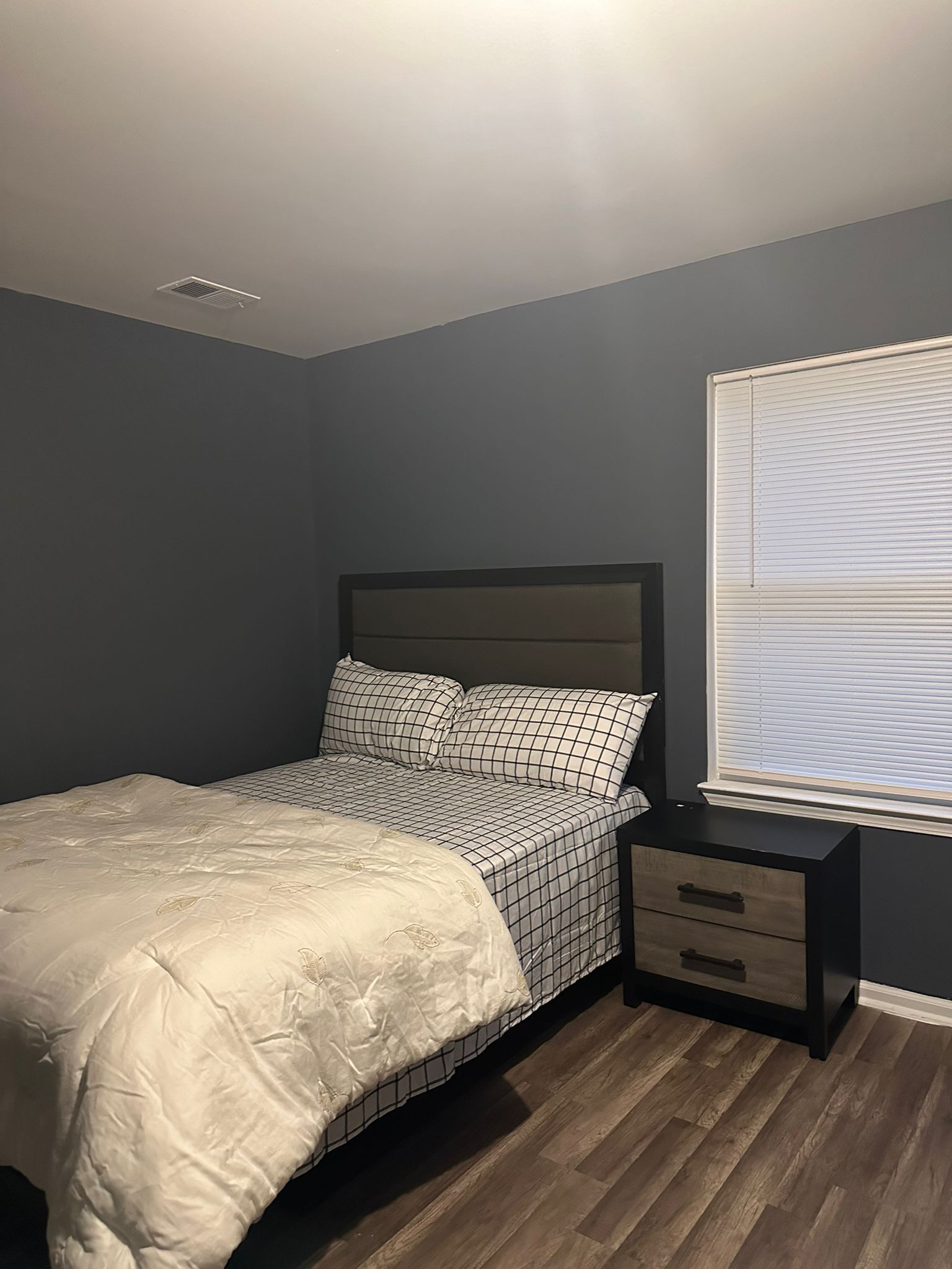 A bedroom with a bed, nightstand, and window with blinds.