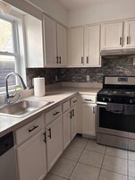 Una cocina con armarios blancos, un lavamanos de acero inoxidable, una estufa empotrada y un salpicadero de piedra.