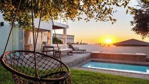 A modern outdoor patio with a pool, lounge chairs, and a hanging chair.