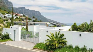 A modern residential area with white buildings, a gated entrance, and a view of a mountain in the background.
