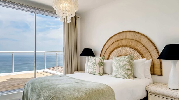 A bedroom with a large bed, a round headboard, two bedside lamps, and a view of the ocean.