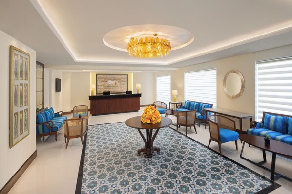 Eine geräumige Lobby mit einem runden Tisch in der Mitte, Teppich mit blau-weißem Muster und einem Kronleuchter.