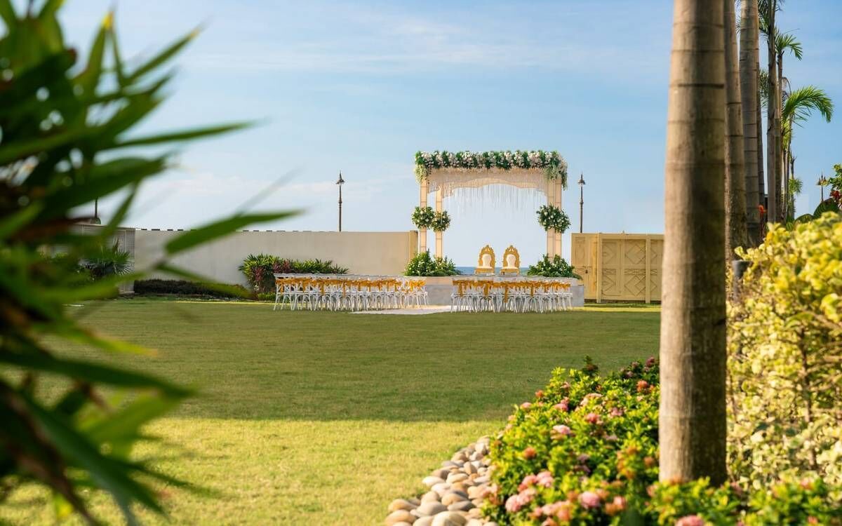 An outdoor wedding venue with a decorated arch, rows of chairs, and a well-maintained lawn.