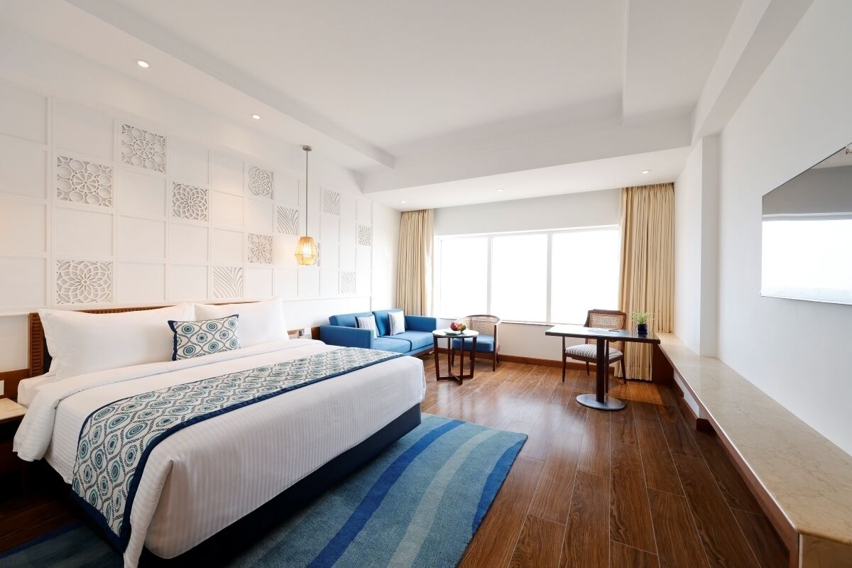 Une chambre d’hôtel moderne avec un grand lit, un canapé bleu, une petite table et une fenêtre avec des rideaux.
