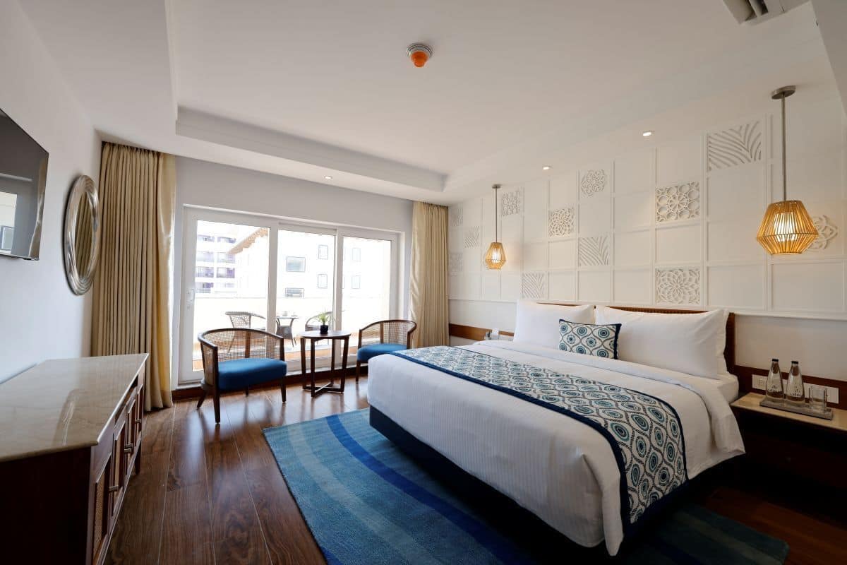 A hotel room with a large bed, a desk, a chair, a window with curtains, and a decorative wall panel.
