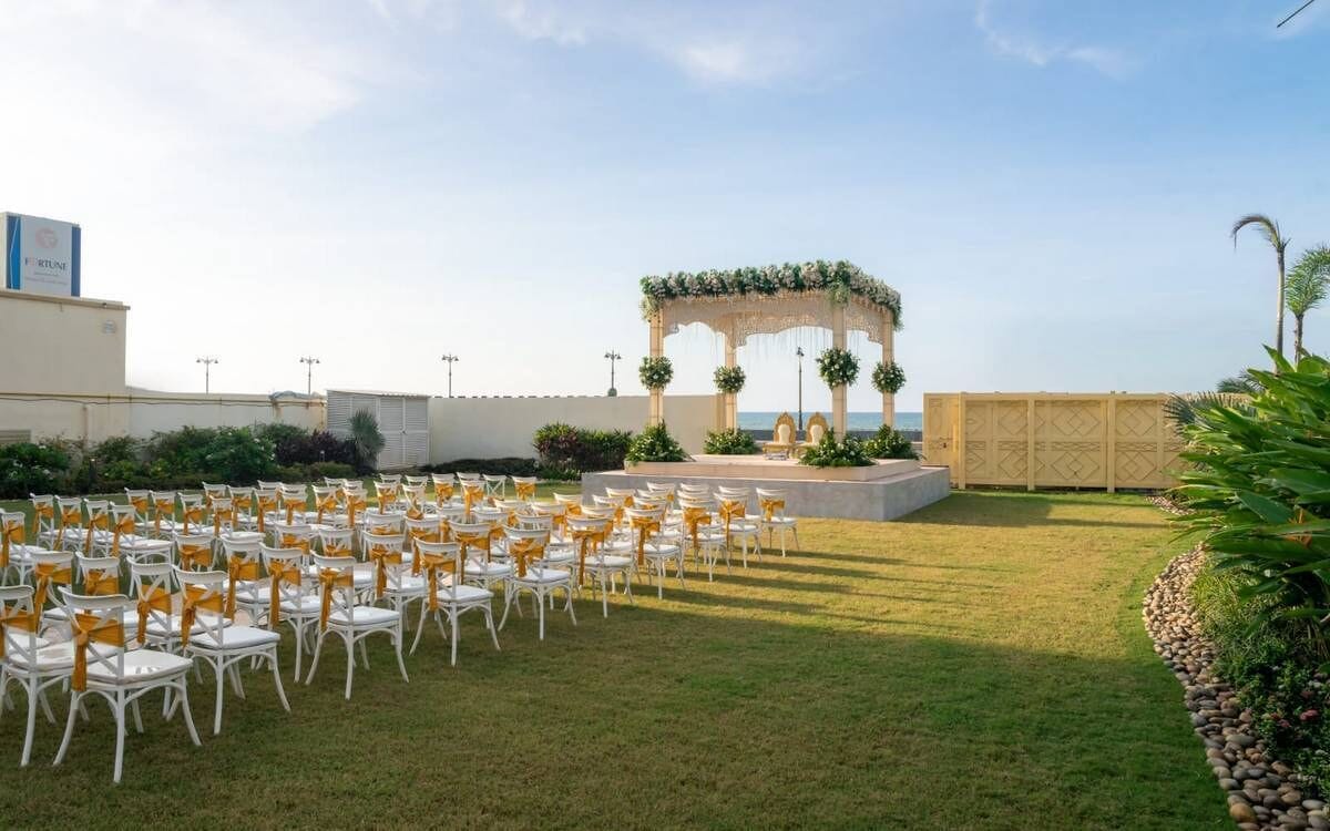 An outdoor wedding venue with white chairs arranged in rows, a decorative arch, and a view of the sea.