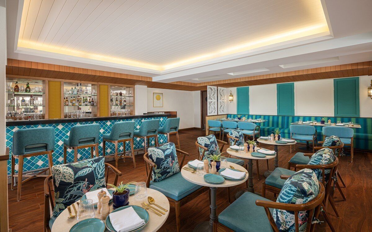A restaurant with multiple seating areas, including booths and round tables, with a bar in the background.