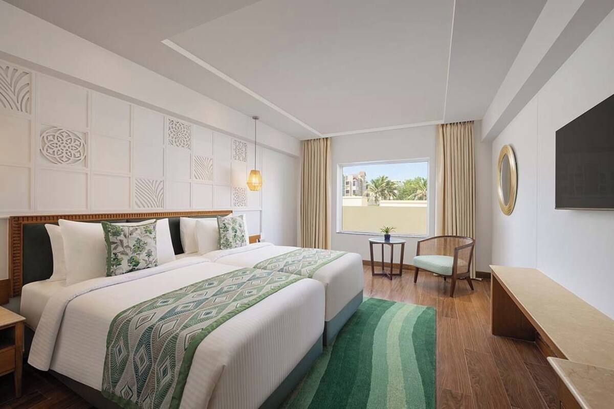 A hotel room with a large bed, a desk, a chair, a TV, and a window with curtains.