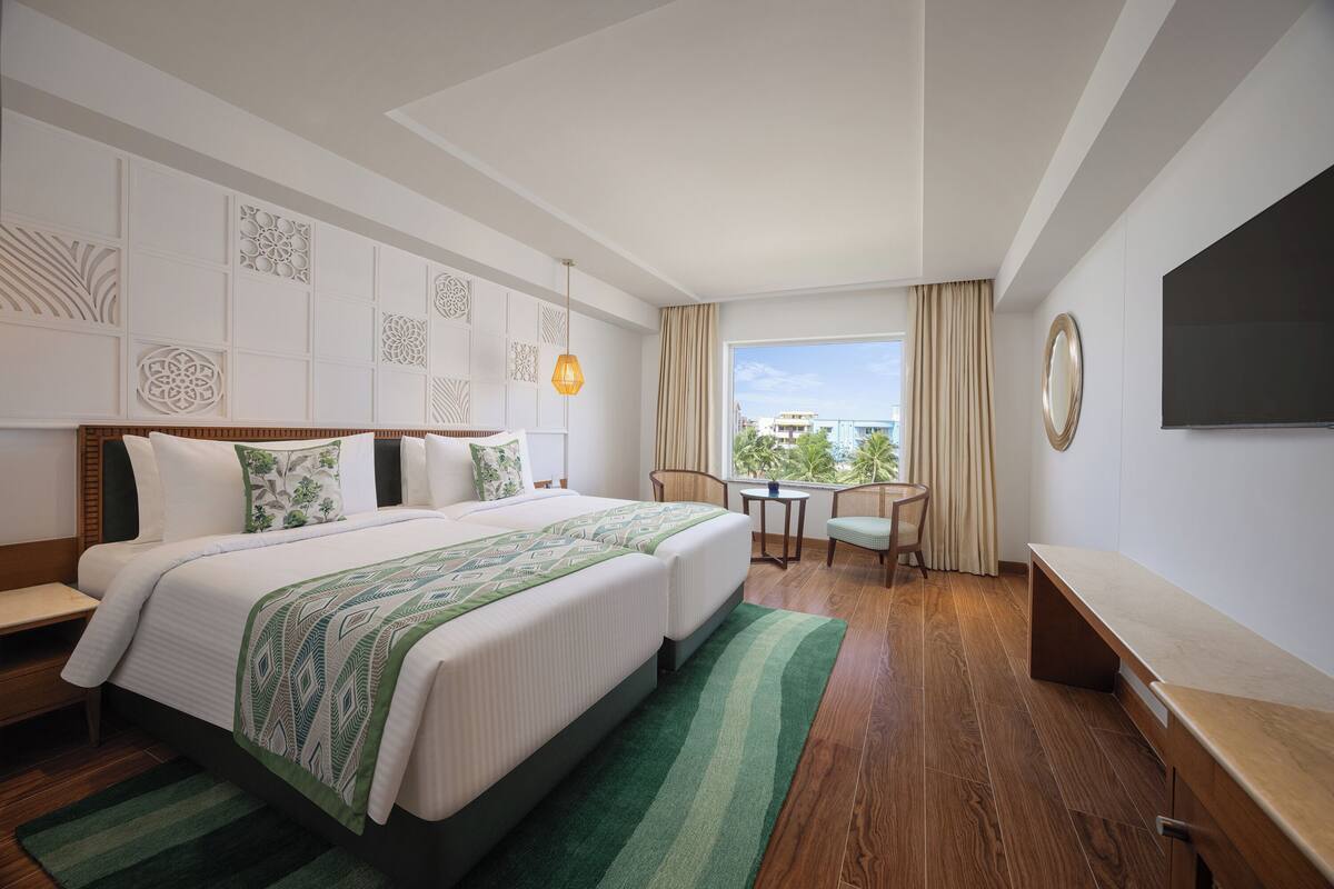 A hotel room with a large bed, a desk, a chair, a TV, and a view of the city.