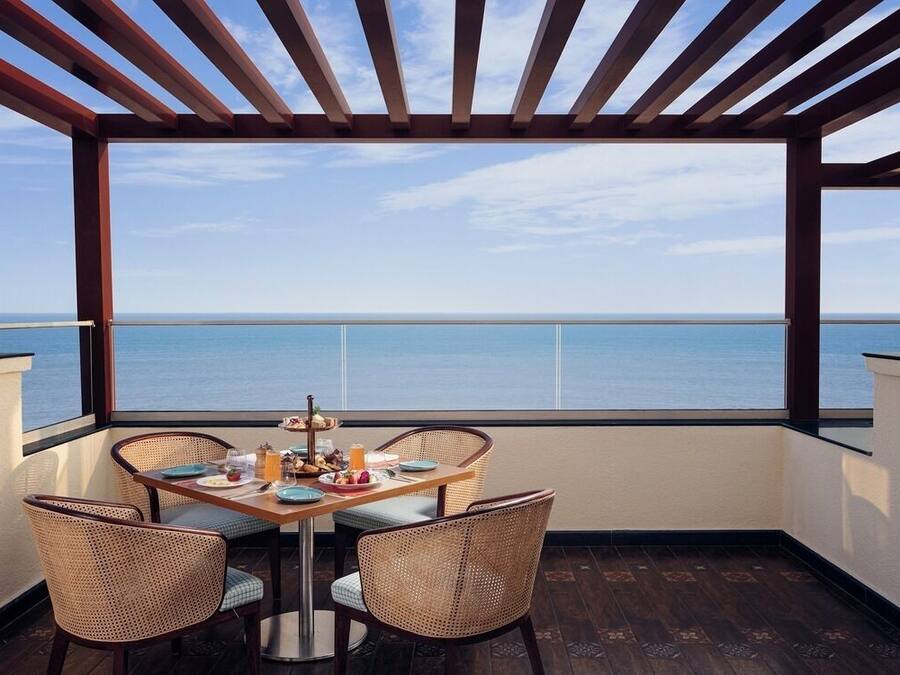 A balcony with a table set for breakfast, wicker chairs, and a view of the sea.