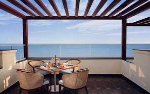 Ein Balkon mit Tisch, gedeckten Tellern für das Frühstück, Korbstühlen und Blick auf das Meer.