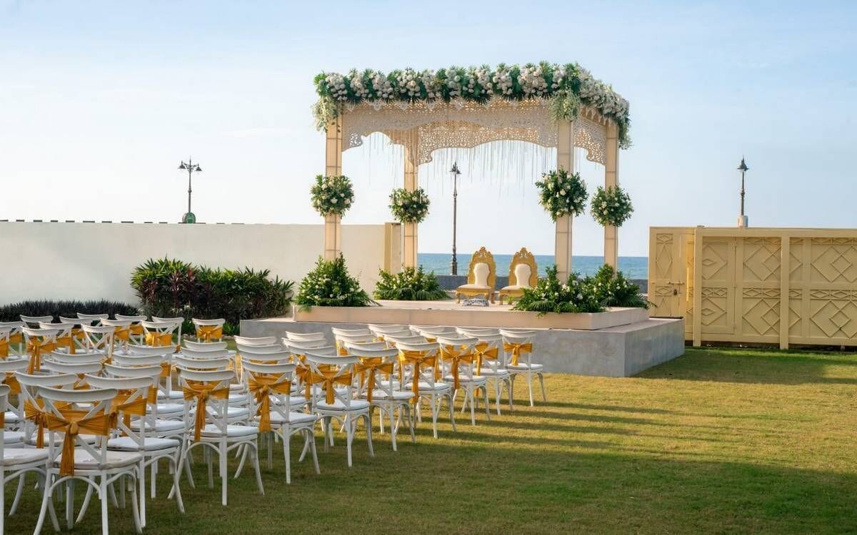 An outdoor wedding setup with a decorated arch, white chairs with yellow sashes, and a view of the sea.