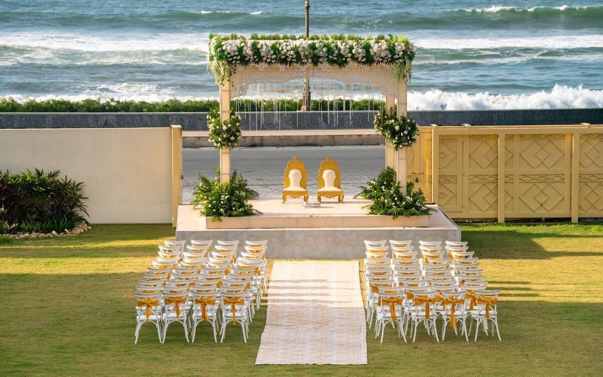 An outdoor wedding setup with a white aisle, chairs with yellow sashes, and a floral arch.