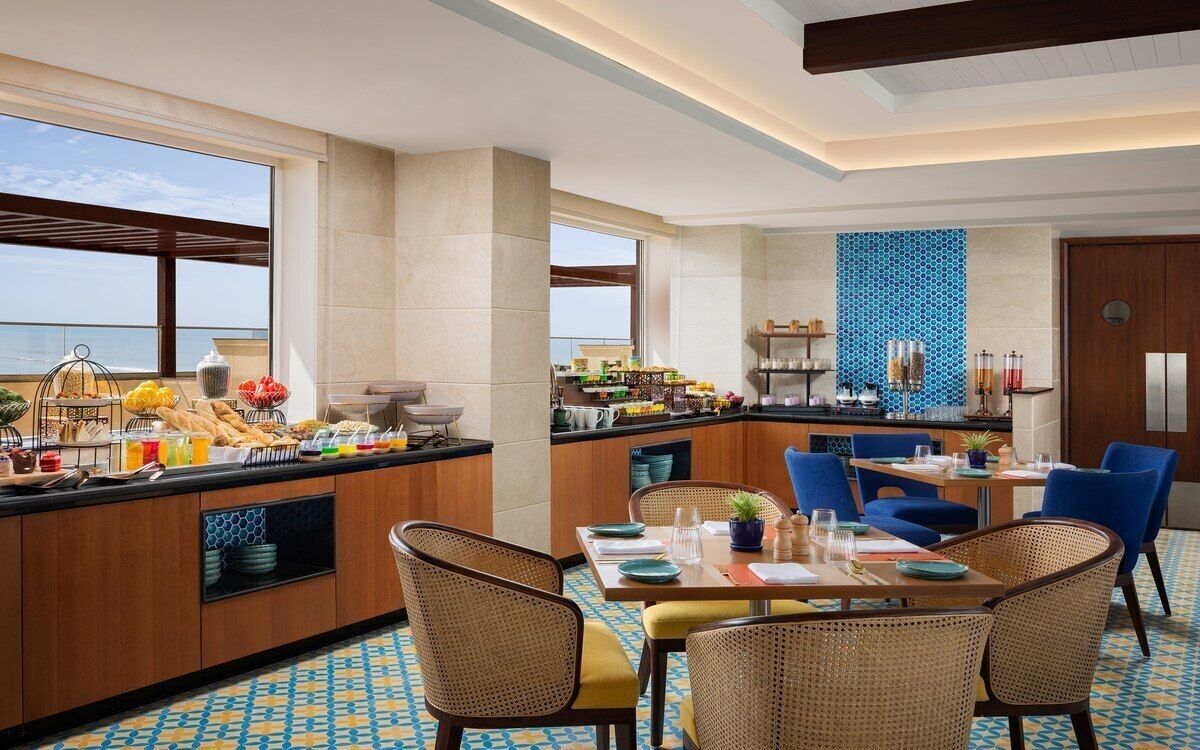 A hotel dining area with a buffet, seating, and a view of the sea.