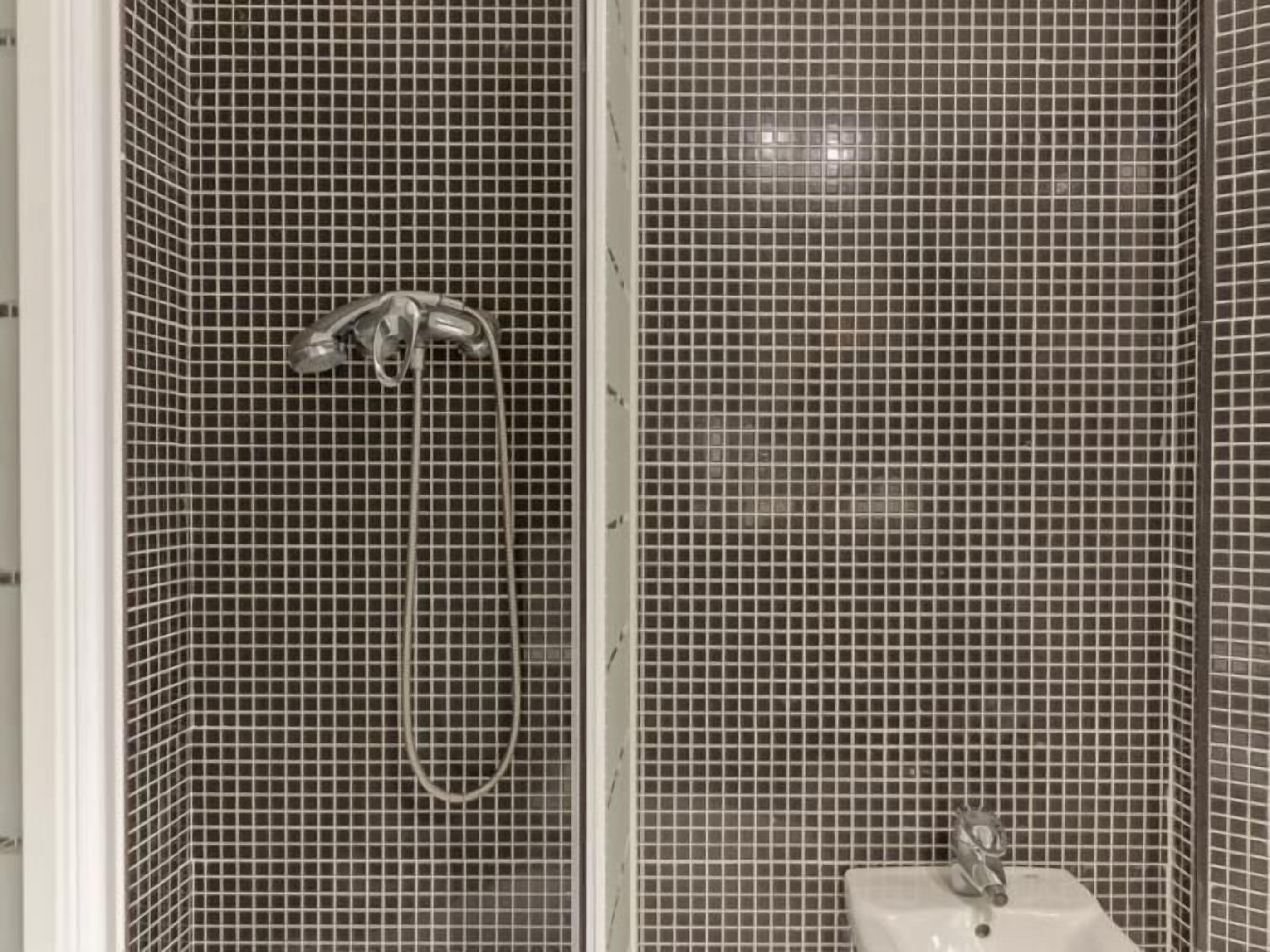 A bathroom with a shower area featuring a tiled wall and a sink with a faucet.