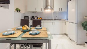 Une cuisine moderne avec des meubles blancs, une hotte en acier inoxydable, un réfrigérateur et une table à manger agrémentée de sets de table et de tasses.
