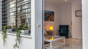 Un salon moderne avec une table basse en verre, un canapé et un fauteuil turquoise. Des plantes en pot sont posées sur le rebord de la fenêtre et un tableau orne le mur.