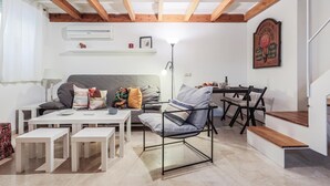 Ein modernes Wohnzimmer mit einer Couch, einem Couchtisch und einem Esstisch. Eine Holztreppe und eine Wandregal mit Dekorationselementen sind ebenfalls vorhanden.