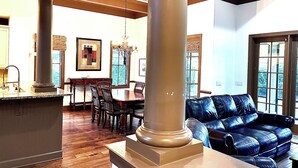 A spacious living room with a large column, a leather sofa, a dining area with wooden chairs, and a chandelier. -  Beautiful 4BR/4BA.Close to HHI/SAV/BEU, 5 minutes to Palmetto Bluff's entrance  (Bluffton)
