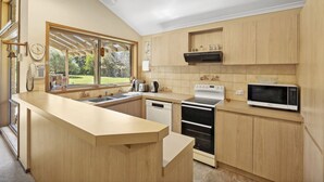 Une cuisine moderne avec des meubles en bois, un four encastré, un four à micro-ondes et une grande fenêtre donnant sur un jardin.