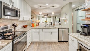 A modern kitchen with white cabinets, stainless steel appliances, and a marble countertop. - Pool & Beach Trolley Access: PCB Resort Condo! (Panama City Beach)