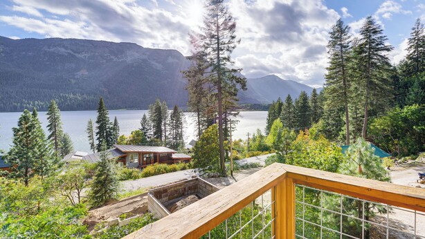 Une cabane dotée d’une terrasse en bois offrant une vue sur un lac et des montagnes.