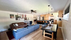A modern living room with a sofa, a dining table, and a kitchen area with wooden cabinets and a bar. - Mid-West Mod-1 mile to OU-Central Norman-Sleeps 16 (Norman)