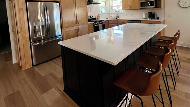 A modern kitchen with wooden cabinets, stainless steel appliances, a large island with bar stools, and pendant lighting. - Mid-West Mod-1 mile to OU-Central Norman-Sleeps 16 (Norman)
