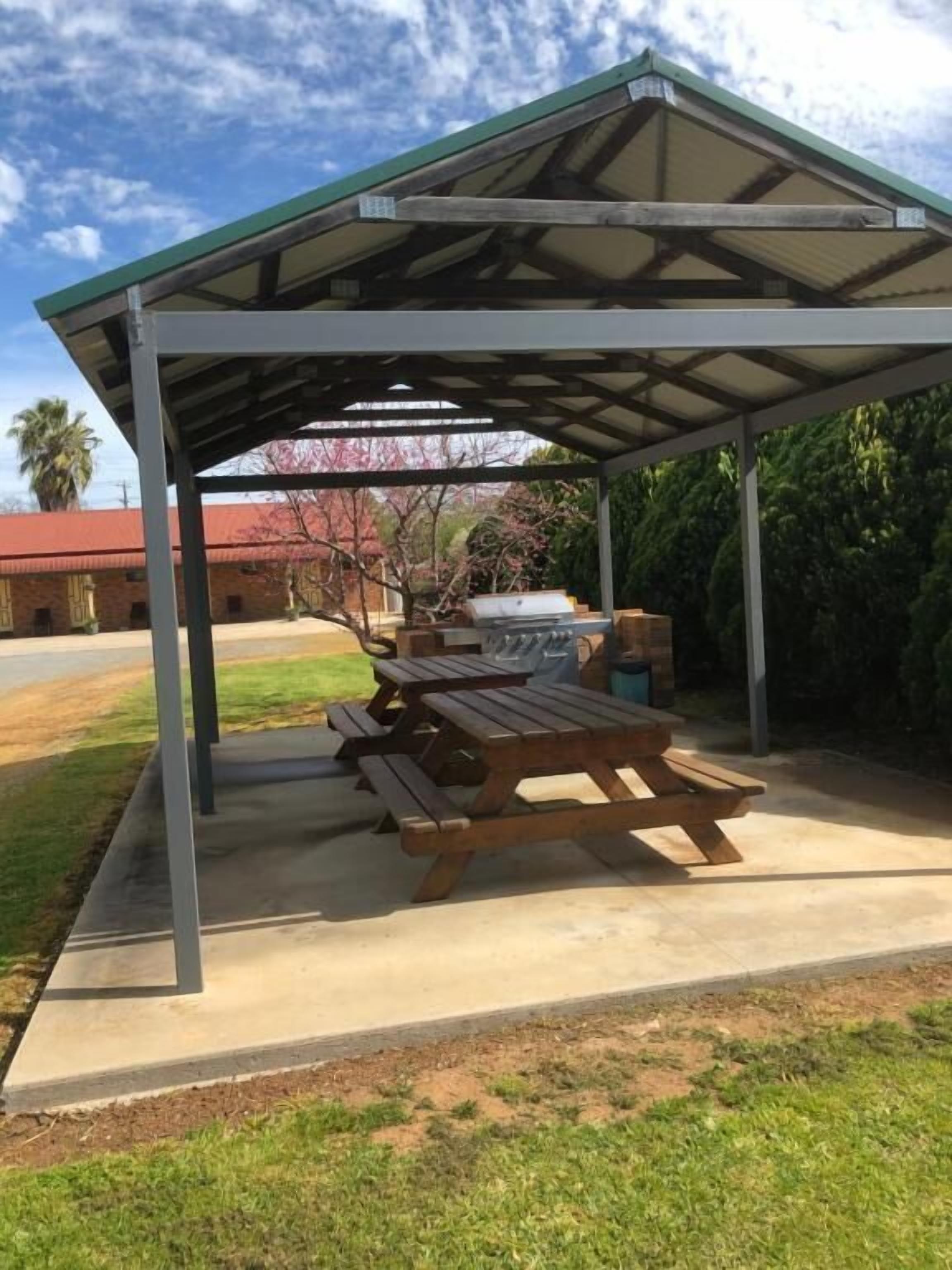 A covered picnic area with a metal roof, concrete floor, and wooden picnic table.