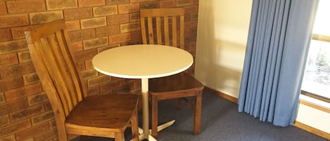 Une petite pièce avec une table ronde et deux chaises en bois, un mur en briques et une fenêtre avec des rideaux.