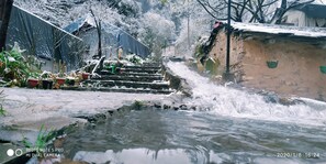 A water feature with cascading water, surrounded by snow-covered plants and a stone pathway. - Hail Himalayas  (Shimla)