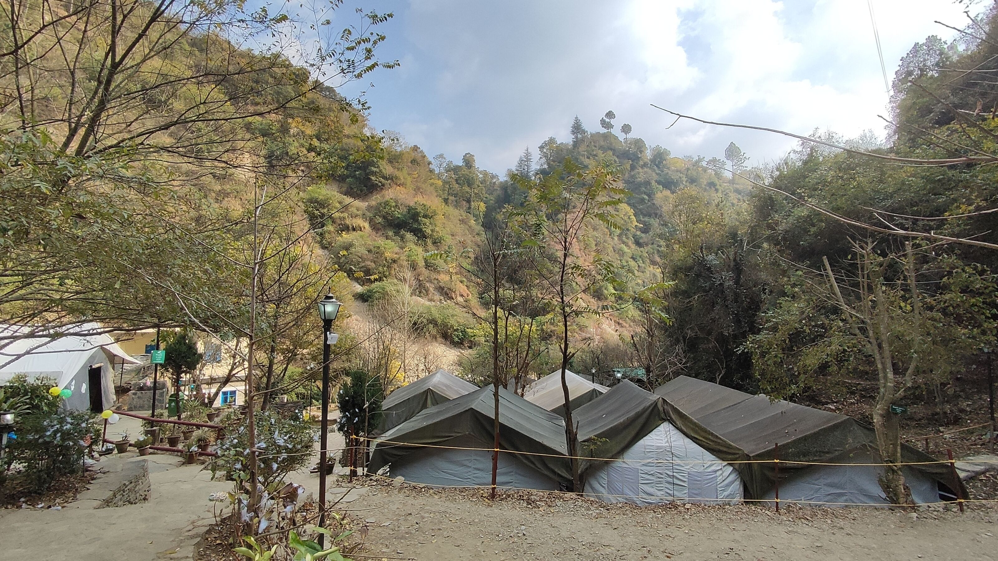 A campsite with tents arranged in rows, surrounded by trees and a hilly landscape.