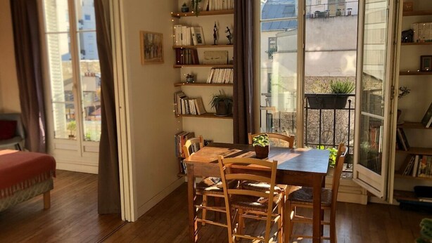 A cozy room with a wooden dining table, chairs, and a bookshelf filled with books and decorative items.