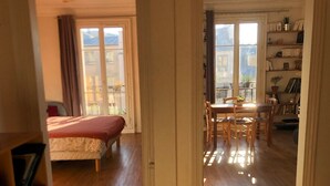 A room with a bed, a dining table with chairs, and a bookshelf.