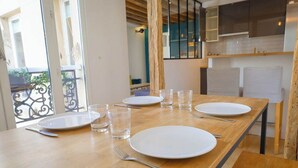 Mesa lista con platos, vasos y cubiertos en una habitación con cocina al fondo.