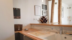 Un baño moderno con encimera de madera, un lavabo y un espejo. Hay cuadros enmarcados en la pared y una guía de vinos.