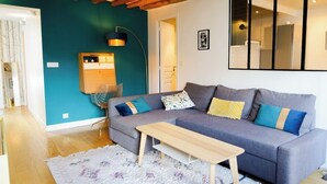 Un salón moderno con un sofá gris, una mesa de centro de madera, paredes color turquesa y una viga de techo de madera.