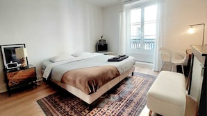 Une chambre à coucher comprenant un lit, un bureau, une chaise, une commode et une fenêtre donnant sur un beau paysage.
